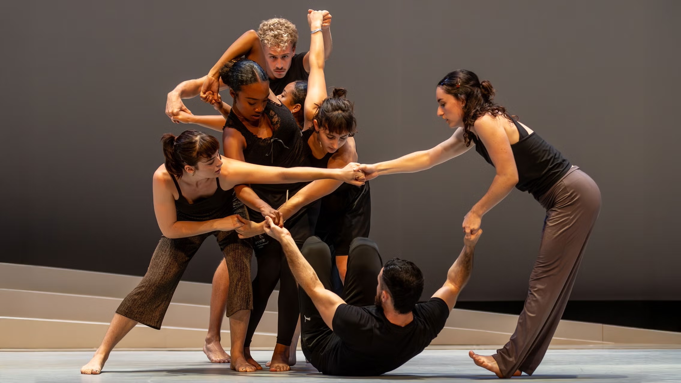 Dancers from Santa Barbara Dance Theater perform "FORUM," linked together in a dynamic and collaborative pose on stage.