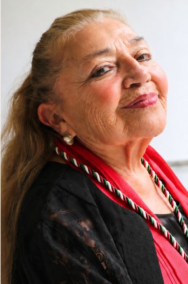 Sara Poot-Herrera smiles for a portrait, wearing a red scarf and pearl earrings.