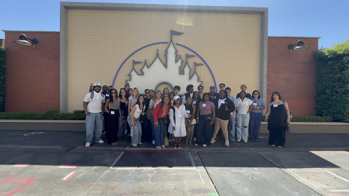 UCSB and Tuskegee summer screenwriting students pose with Disney development executives in front of a Disney castle backdrop during a behind-the-scenes visit.